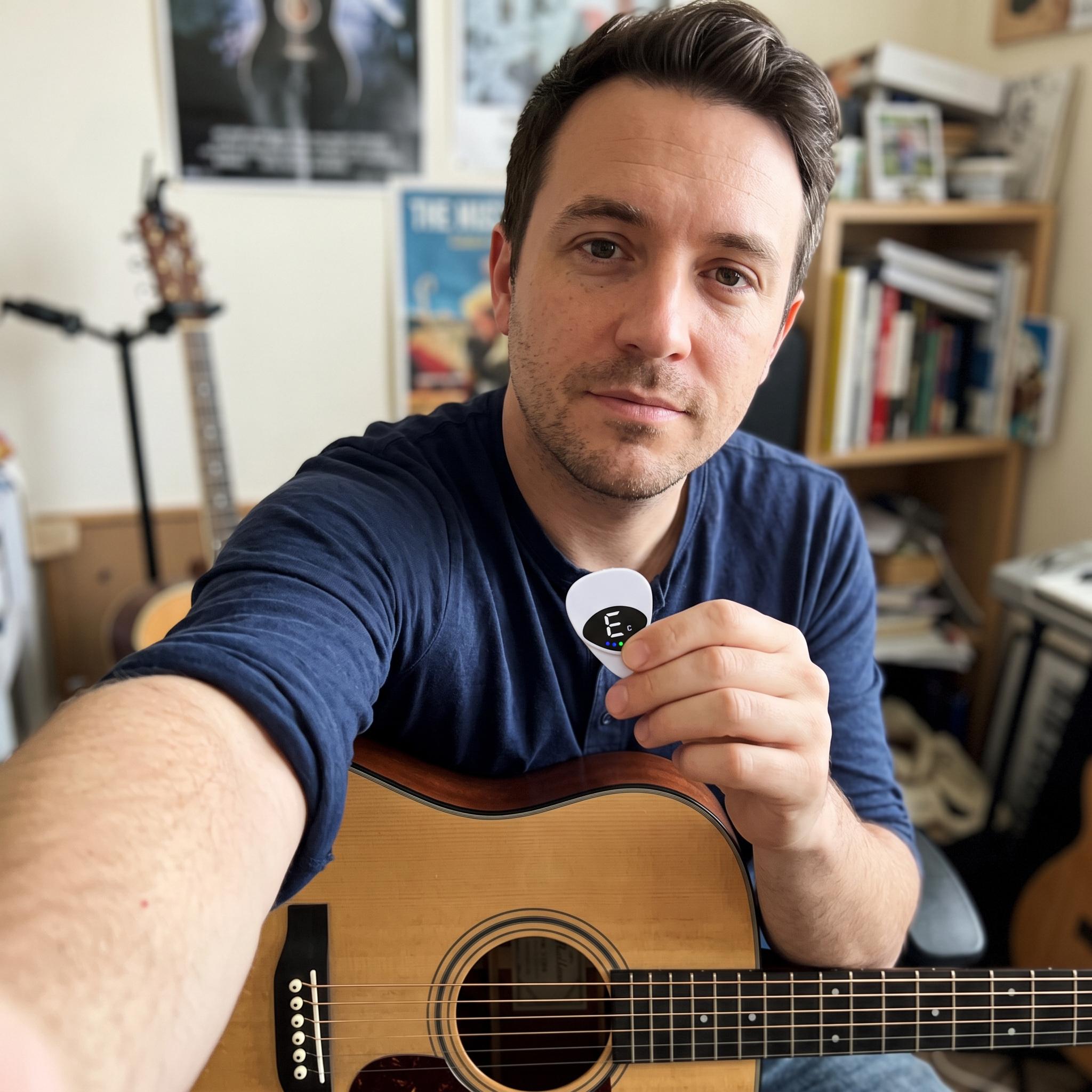 Man in a navy shirt holding Chordwell beside an acoustic guitar